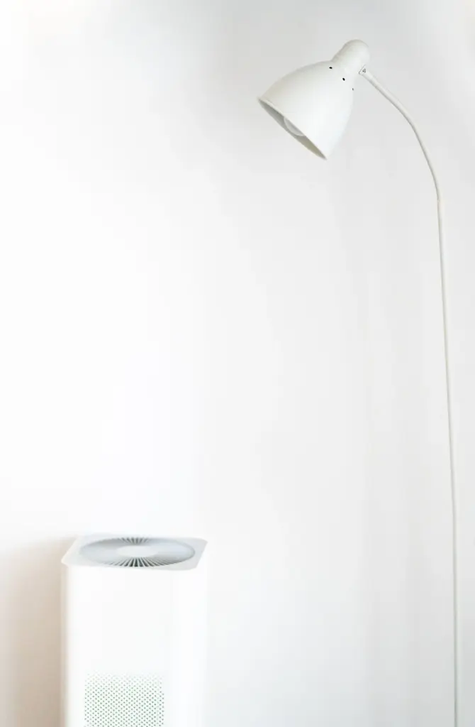 White portable air purifier beside a floor lamp in a simple room