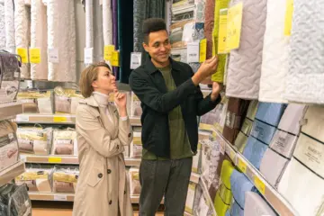Couple comparing quilted bedding and price labels in a store