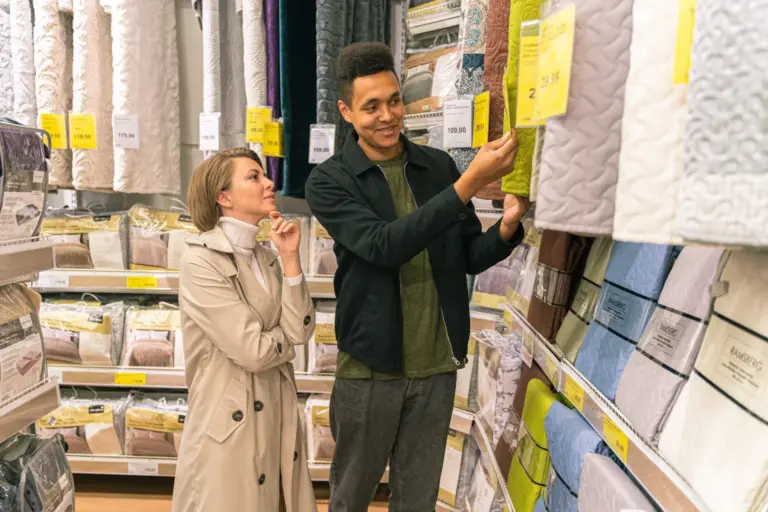 Couple comparing quilted bedding and price labels in a store