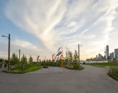 Paths and young trees in Biidaasige Park at sunset with Toronto skyline in the distance