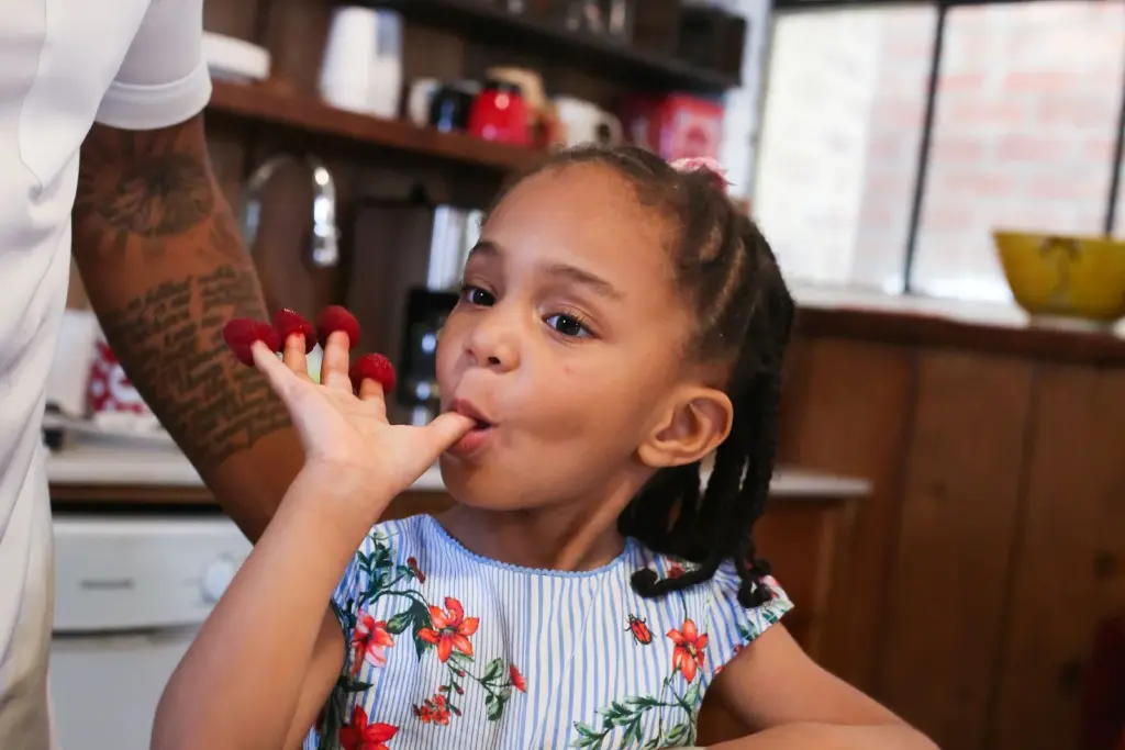 Young child eating raspberries at a kitchen table