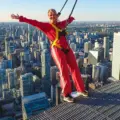 A woman in a red EdgeWalk suit leans above downtown Toronto