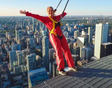A woman in a red EdgeWalk suit leans above downtown Toronto