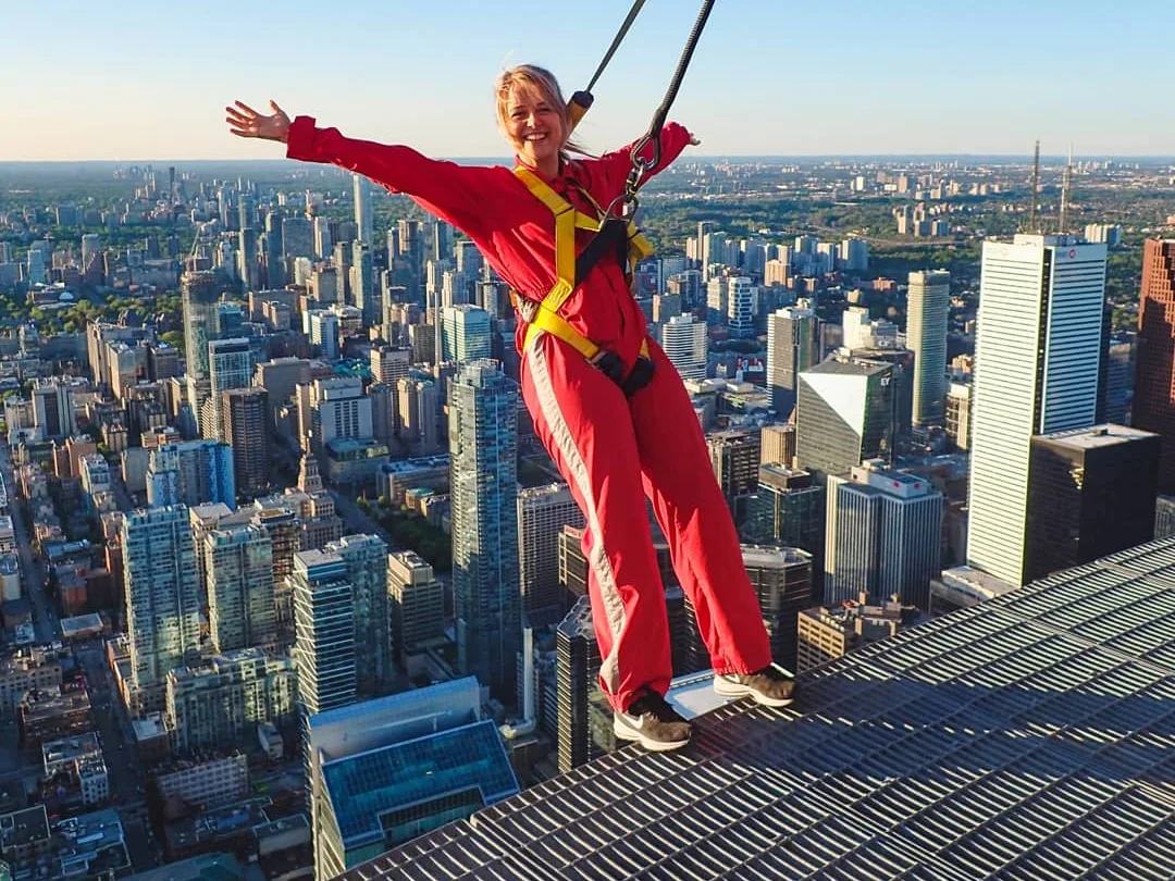 A woman in a red EdgeWalk suit leans above downtown Toronto
