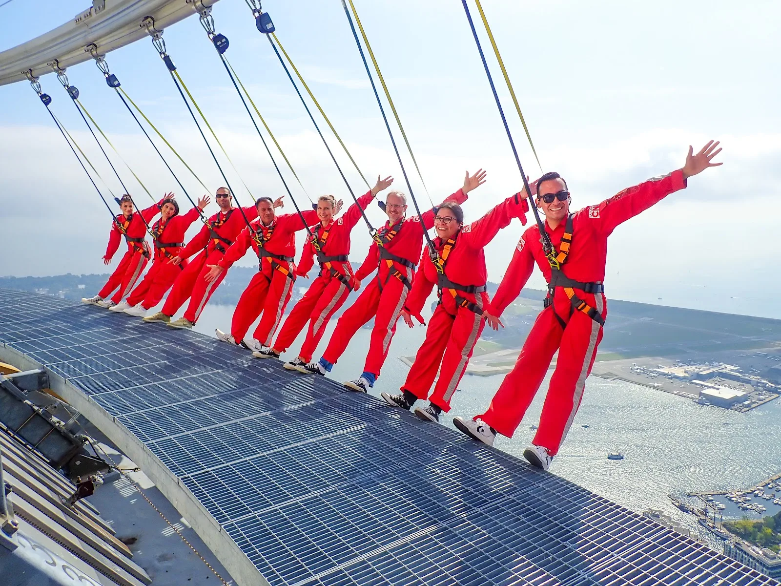 A group in red EdgeWalk suits leans together over the city