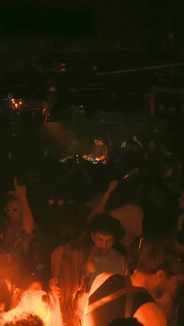 People dance with their hands raised behind the DJ booth at CODA Toronto.