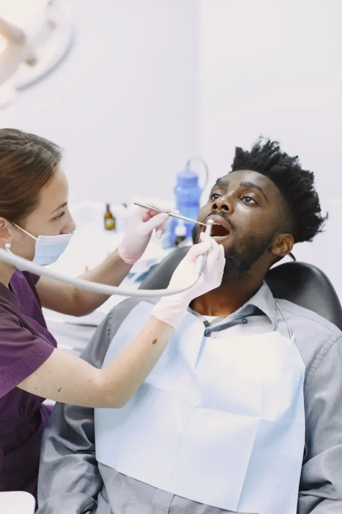 Female dentist performing a routine checkup for a Black male patient