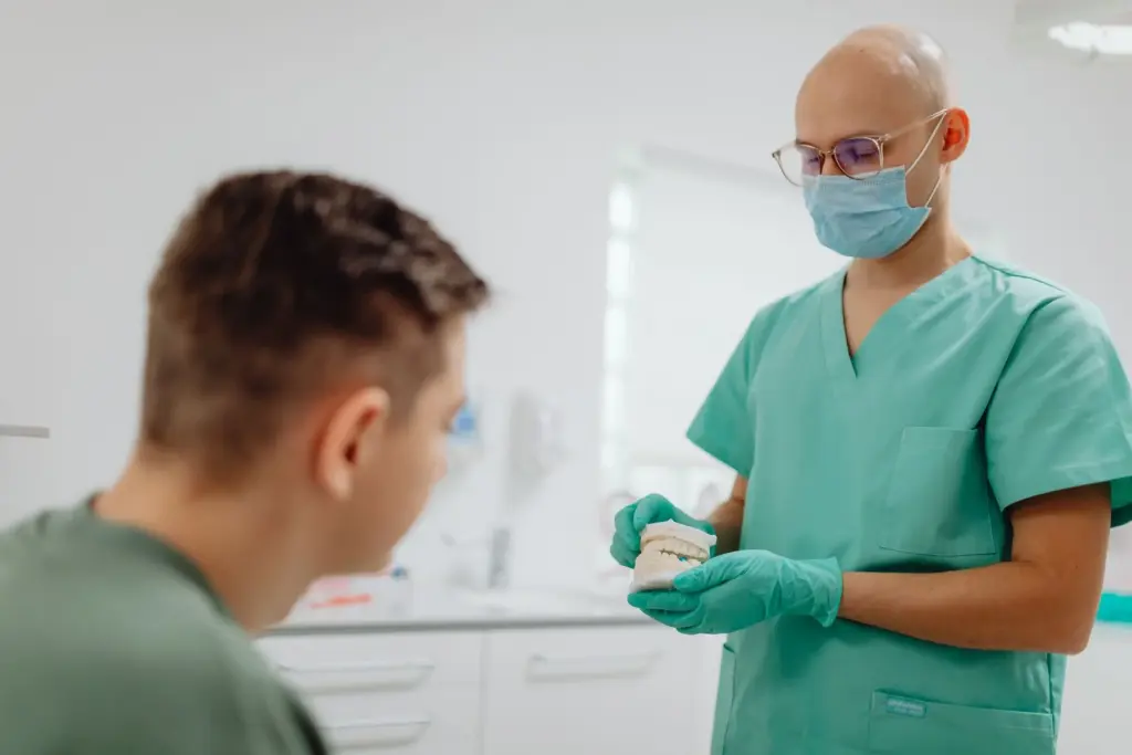 Dentist in green scrubs using a dental model while speaking with a patient