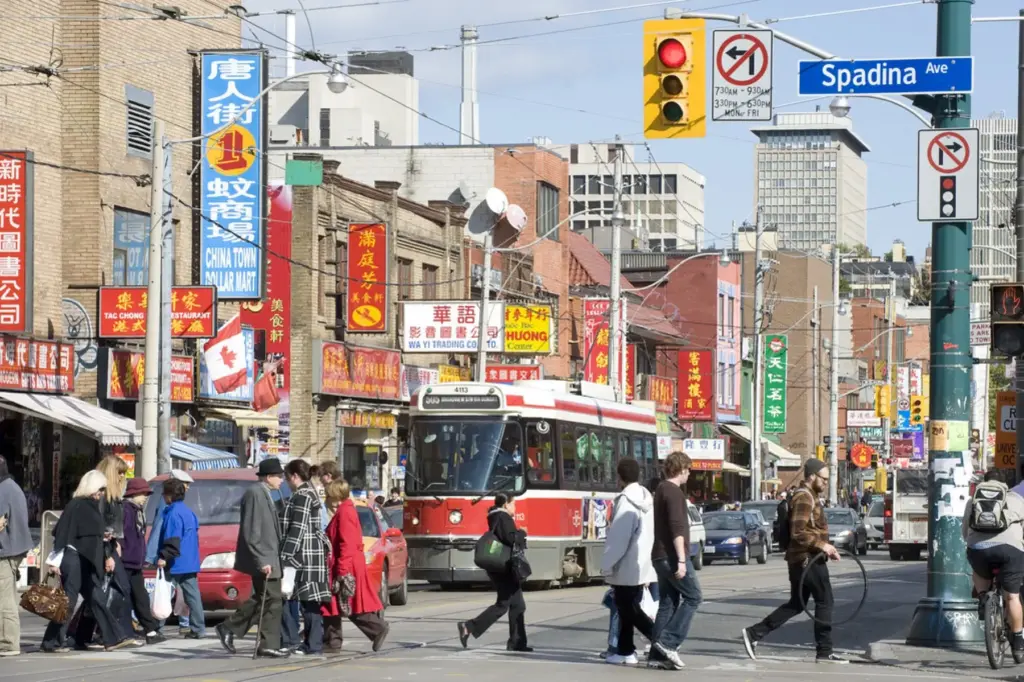 Pedestrians crossing Spadina Avenue with a TTC streetcar and Chinatown shops behind them