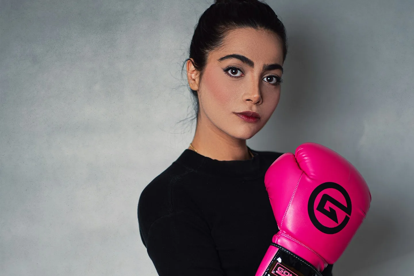 A woman wearing bright pink boxing gloves stands ready to train