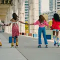 Four women from different backgrounds holding hands while roller skating beneath the Gardiner at The Bentway in Toronto