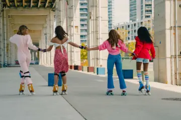 Four women from different backgrounds holding hands while roller skating beneath the Gardiner at The Bentway in Toronto