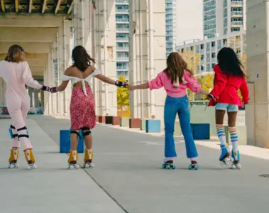 Four women from different backgrounds holding hands while roller skating beneath the Gardiner at The Bentway in Toronto