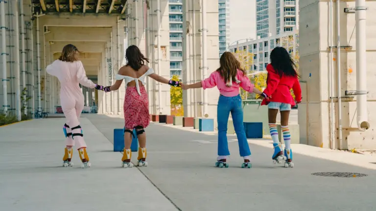 Four women from different backgrounds holding hands while roller skating beneath the Gardiner at The Bentway in Toronto