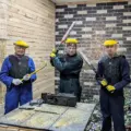 Three guests in protective gear pose with tools inside Go Smash Canada