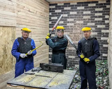 Three guests in protective gear pose with tools inside Go Smash Canada