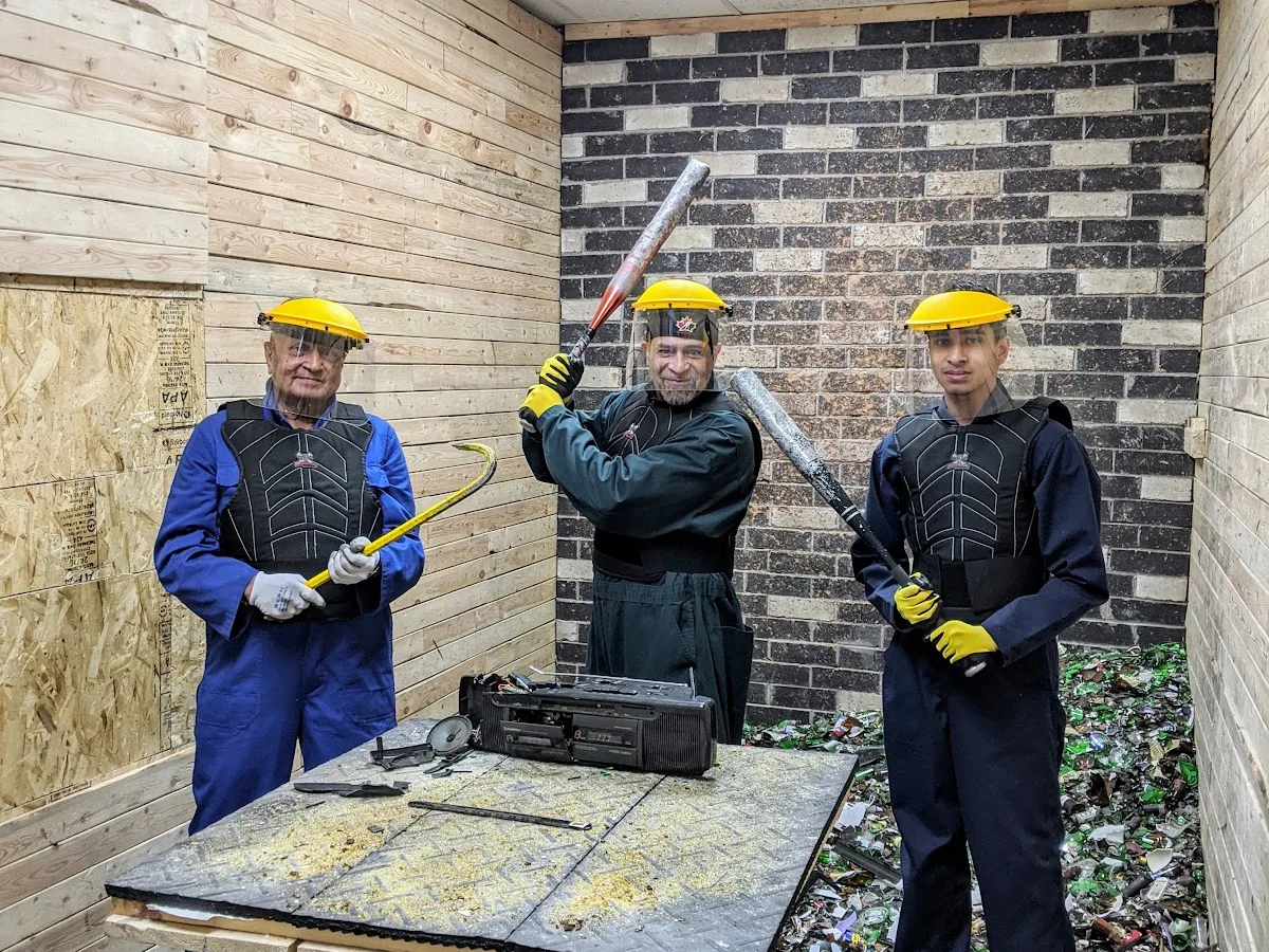 Three guests in protective gear pose with tools inside Go Smash Canada