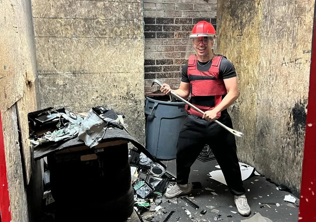A guest in protective gear holds a metal bar inside the Go Smash rage room