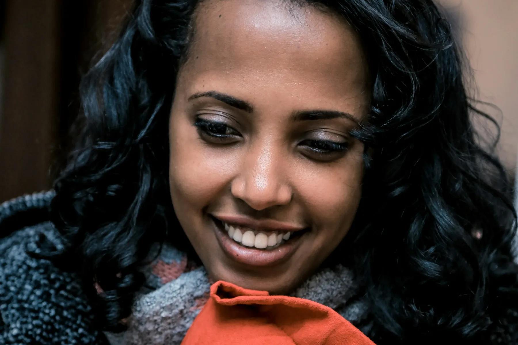 A woman smiles while holding an orange pillow close to her face