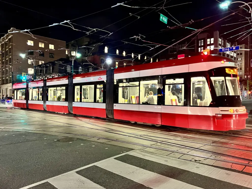 Red and white TTC streetcar at Spadina Avenue and King Street at night