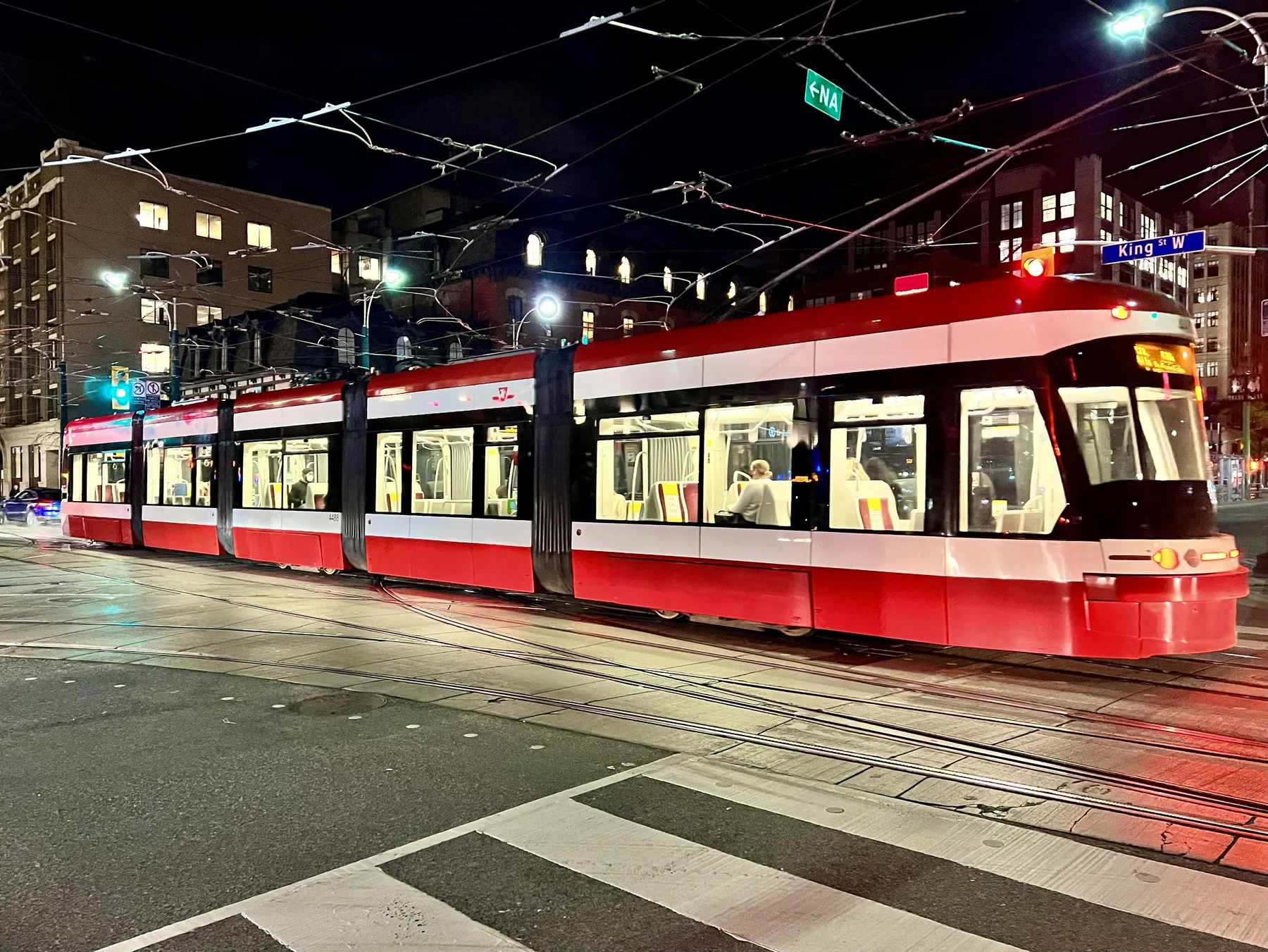 Red and white TTC streetcar at Spadina Avenue and King Street at night