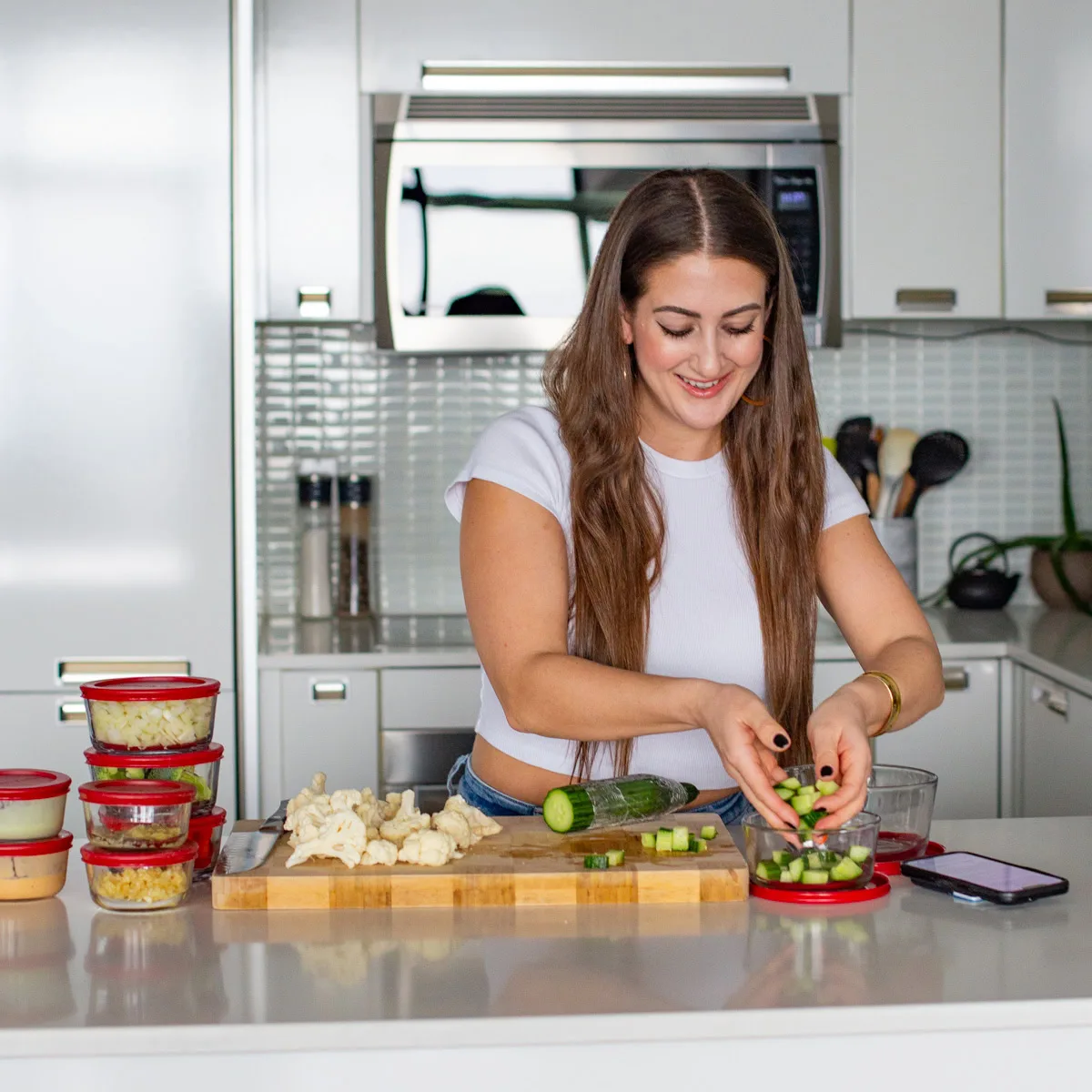 Woman chopping vegetables and arranging meal-prep containers in a bright kitchen