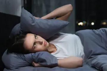 Woman covering her ears with a pillow while trying to sleep