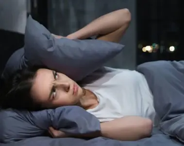 Woman covering her ears with a pillow while trying to sleep