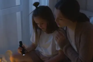 A mother and daughter reading together by flashlight during a power outage