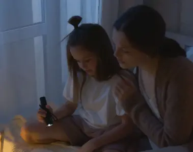 A mother and daughter reading together by flashlight during a power outage