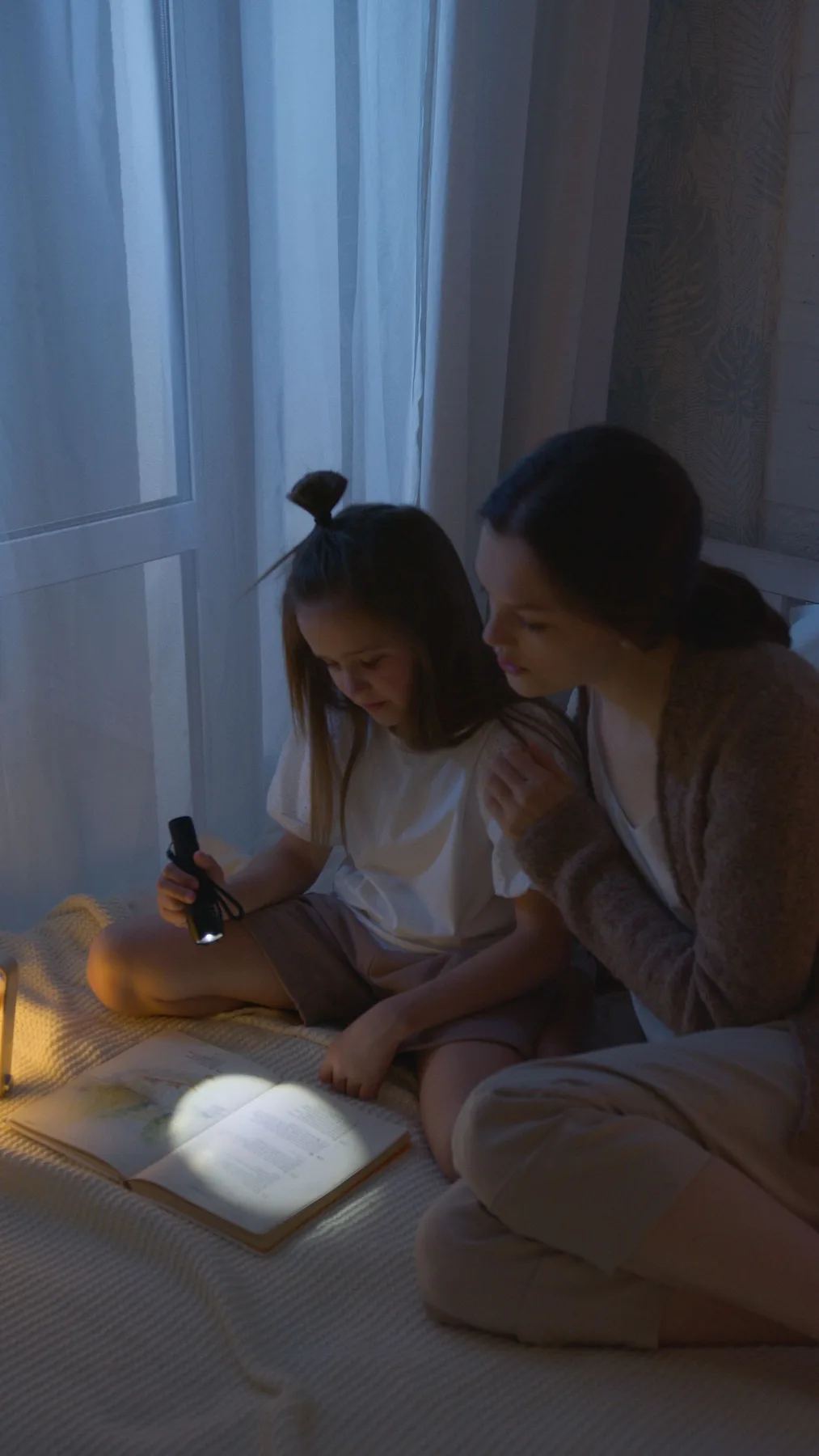 A mother and daughter reading together by flashlight during a power outage