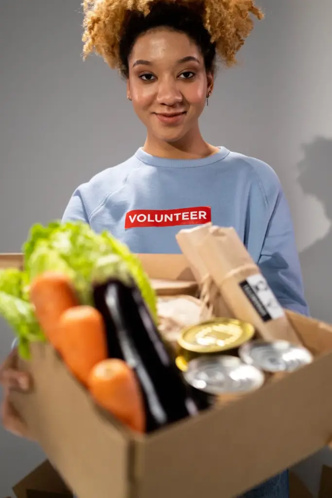 A woman holding a donation box filled with vegetables and canned food
