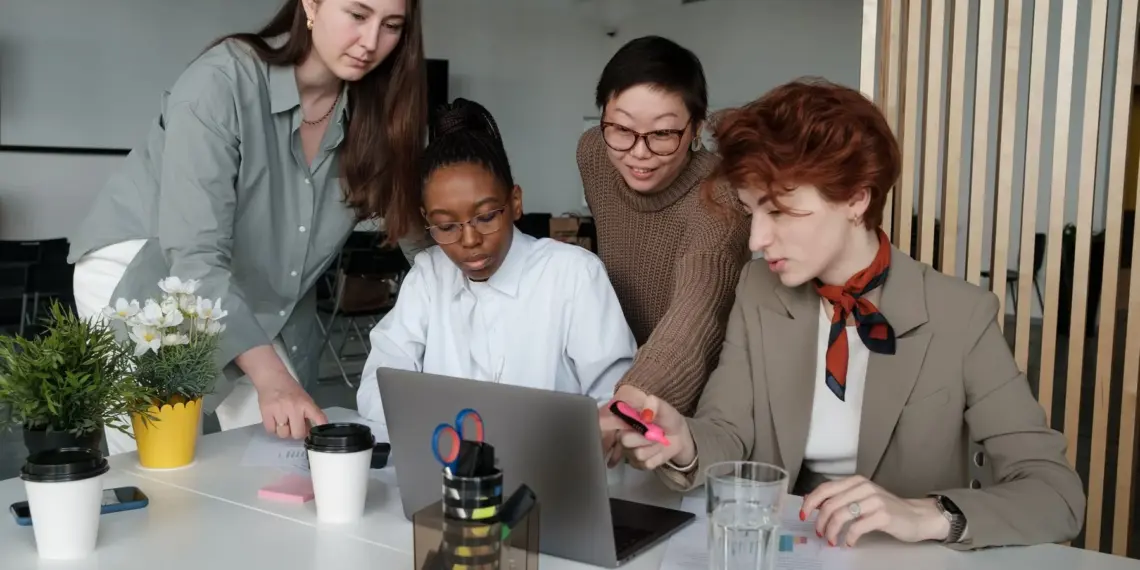Women reviewing work together around a laptop in a bright office