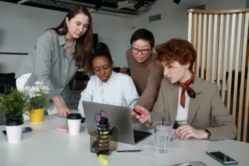 Women reviewing work together around a laptop in a bright office