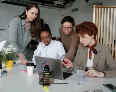 Women reviewing work together around a laptop in a bright office