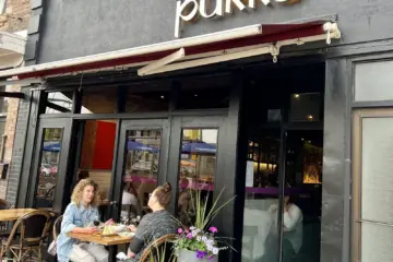 Two women dining on the flower-filled patio at Pukka on St. Clair West in Toronto