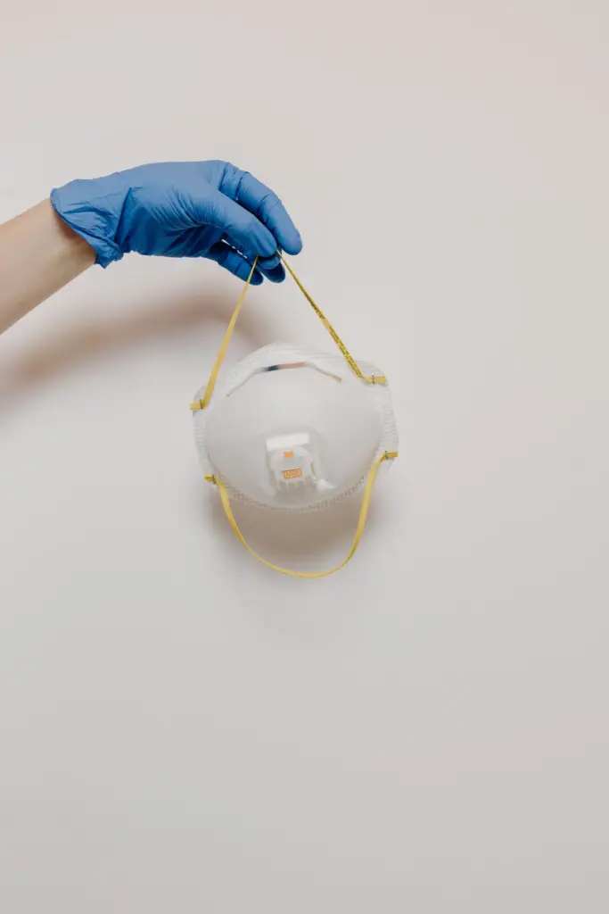 Blue gloved hand holding a cup-style N95 respirator