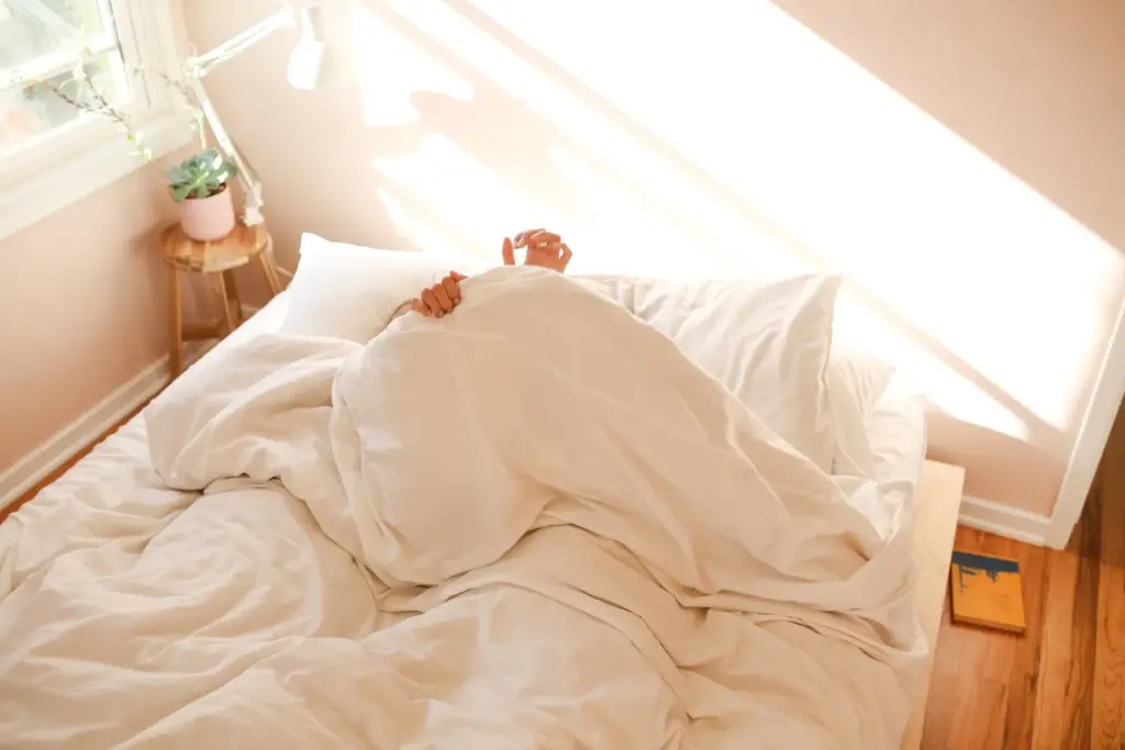 Person resting under a white duvet in a bright bedroom