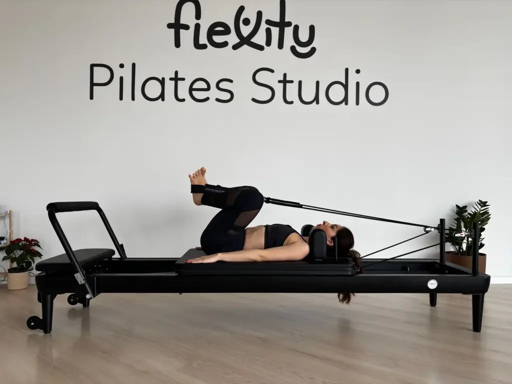 Woman using resistance straps while lying on a Pilates reformer