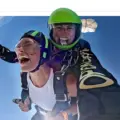 A smiling tandem skydiver gives a thumbs-up during freefall