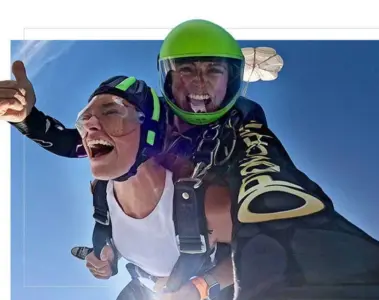 A smiling tandem skydiver gives a thumbs-up during freefall