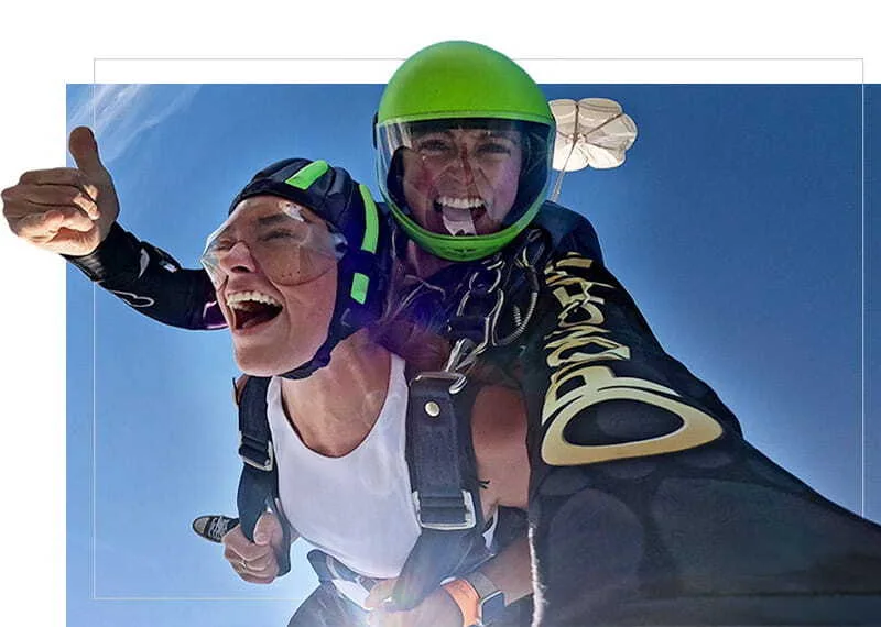 A smiling tandem skydiver gives a thumbs-up during freefall