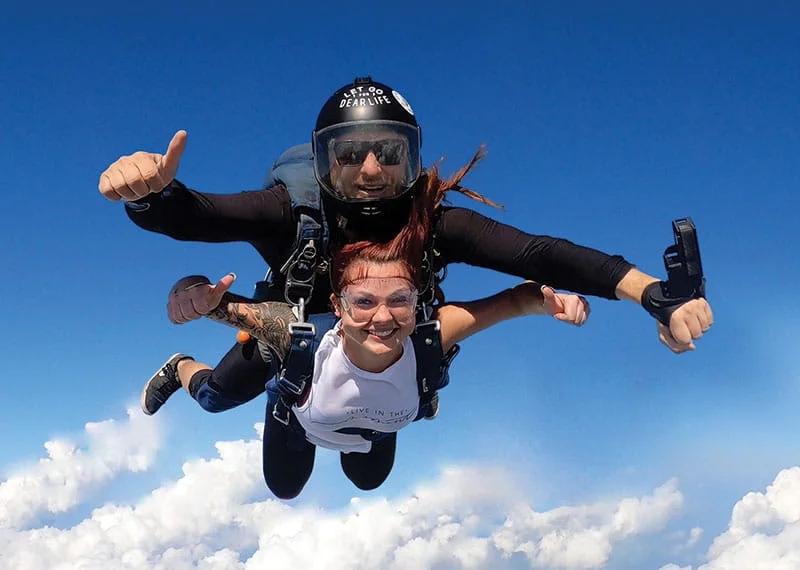 A tandem skydiver spreads her arms above the clouds