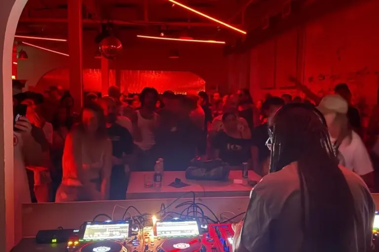 A DJ faces a crowded dance floor under red lights at Standard Time on Geary Avenue.