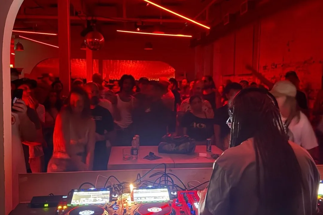 A DJ faces a crowded dance floor under red lights at Standard Time on Geary Avenue.