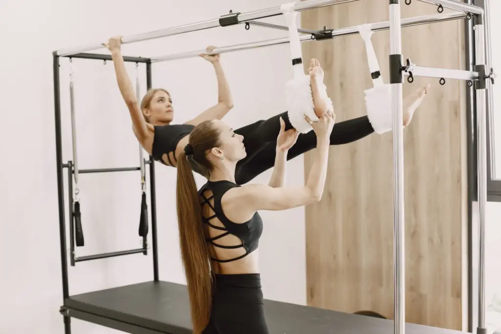 Two women using Pilates tower equipment in a bright studio