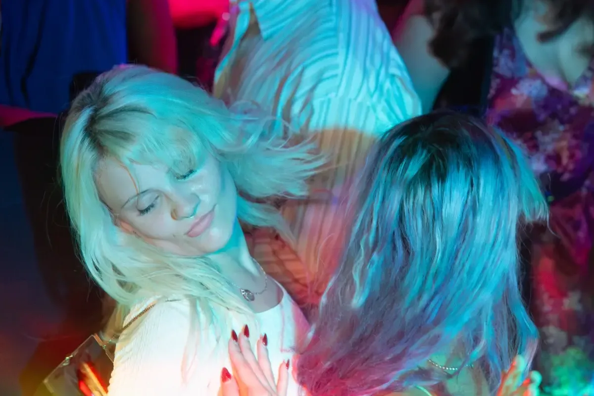 Two women dance under blue and pink lights at the Wax Candy party inside The Piston.