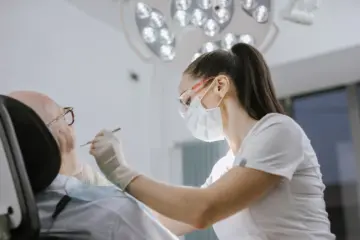 Female dentist wearing a mask while examining an older patient in a bright clinic