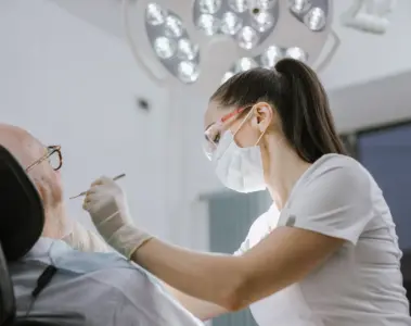 Female dentist wearing a mask while examining an older patient in a bright clinic