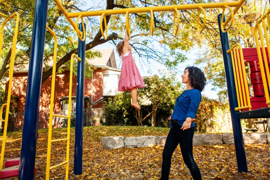 Mother helping a young child climb at a Toronto playground in autumn